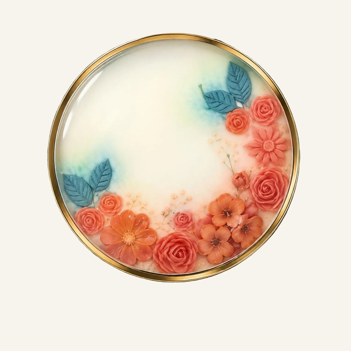 A round decorative plate with a gold rim, featuring pressed flowers and blue-green leaves arranged around a cream center, presented in a black square box on a white background.